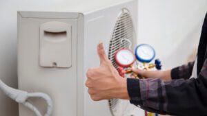 A technician is using measuring equipment to check an HVAC unit and giving a thumbs-up sign
