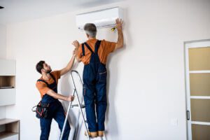 two men working on a wall ac unit