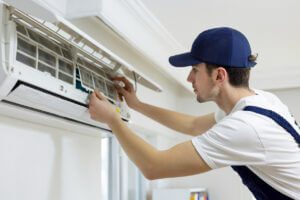 AC water leakage - a male technician fixing an air conditioner unit inside a home.