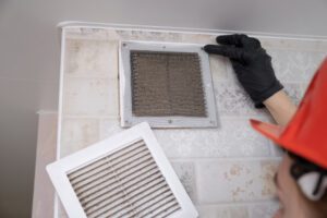 A professional worker in a protective suit and helmet cleans the Ventilation grill. Flat Panel Fiberglass Filters Of Central Air Condition System With Dust